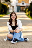 A high school senior girl sits on a walkway smiling for a senior portrait.