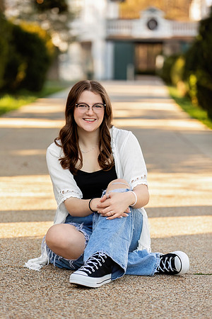 A high school senior girl sits on a walkway smiling for a senior portrait.
